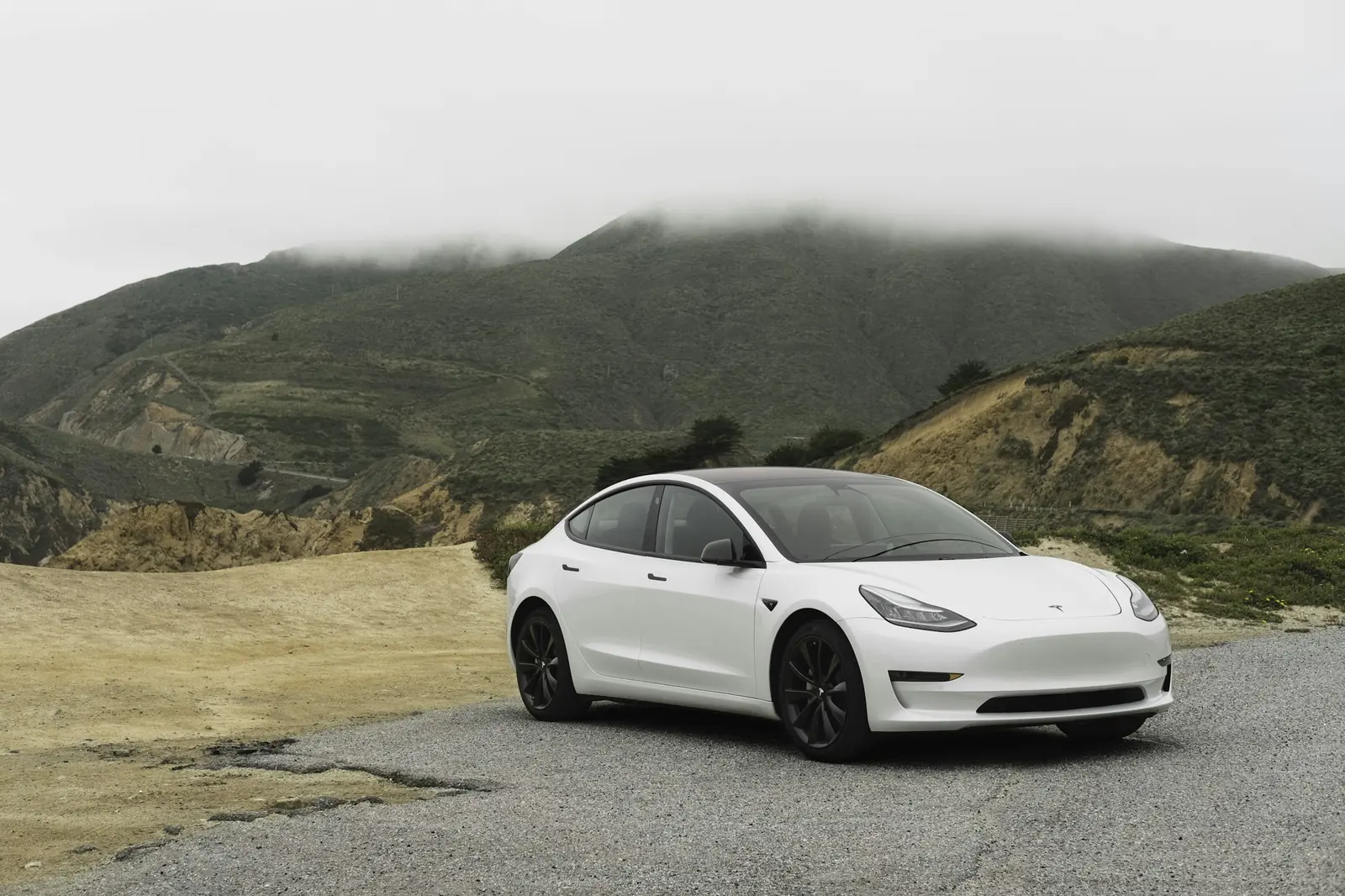A white electric sedan on a road beneath green hills