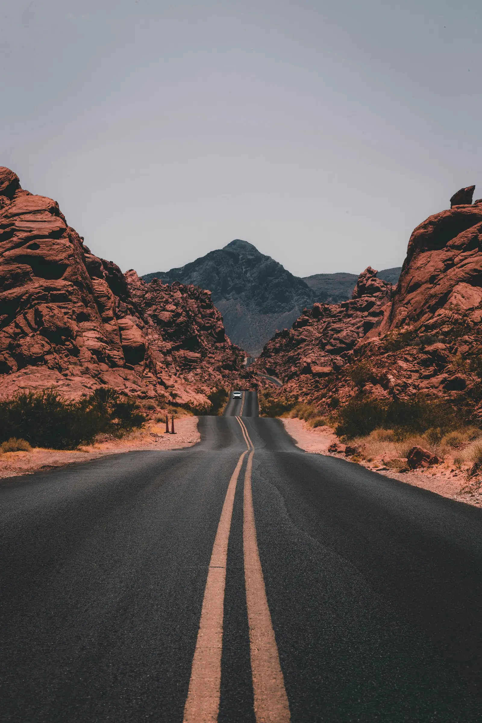A two-lane road running through red rock toward a distant peak