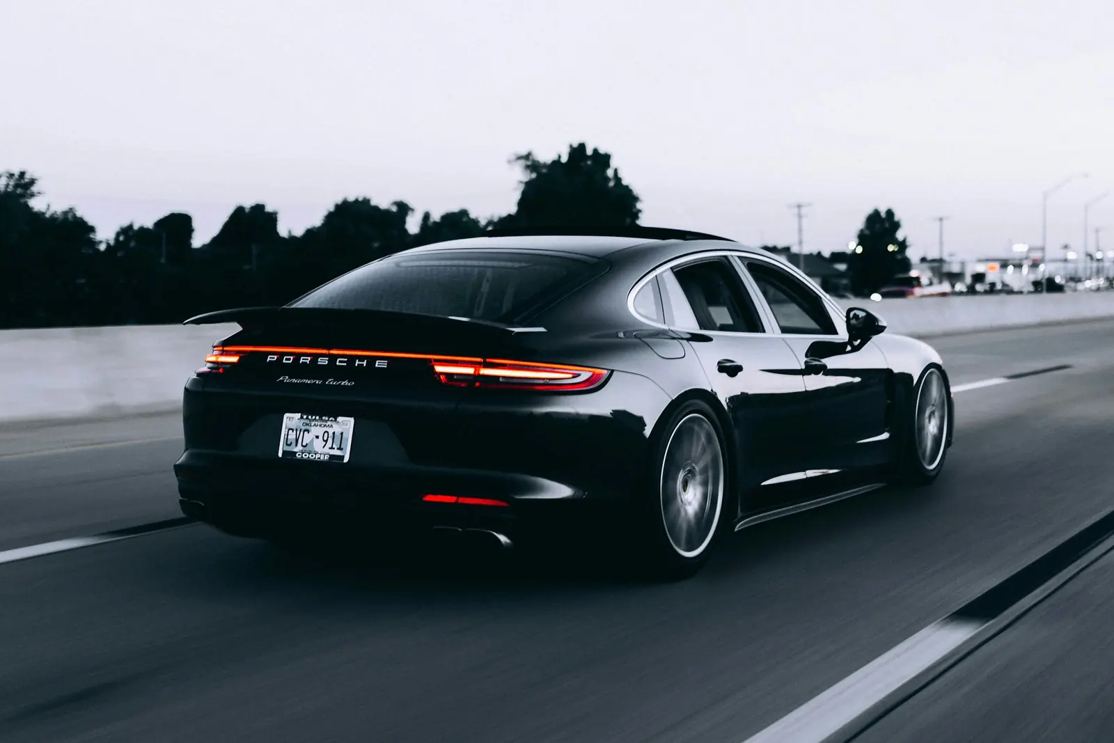 A black coupe driving on a highway at dusk